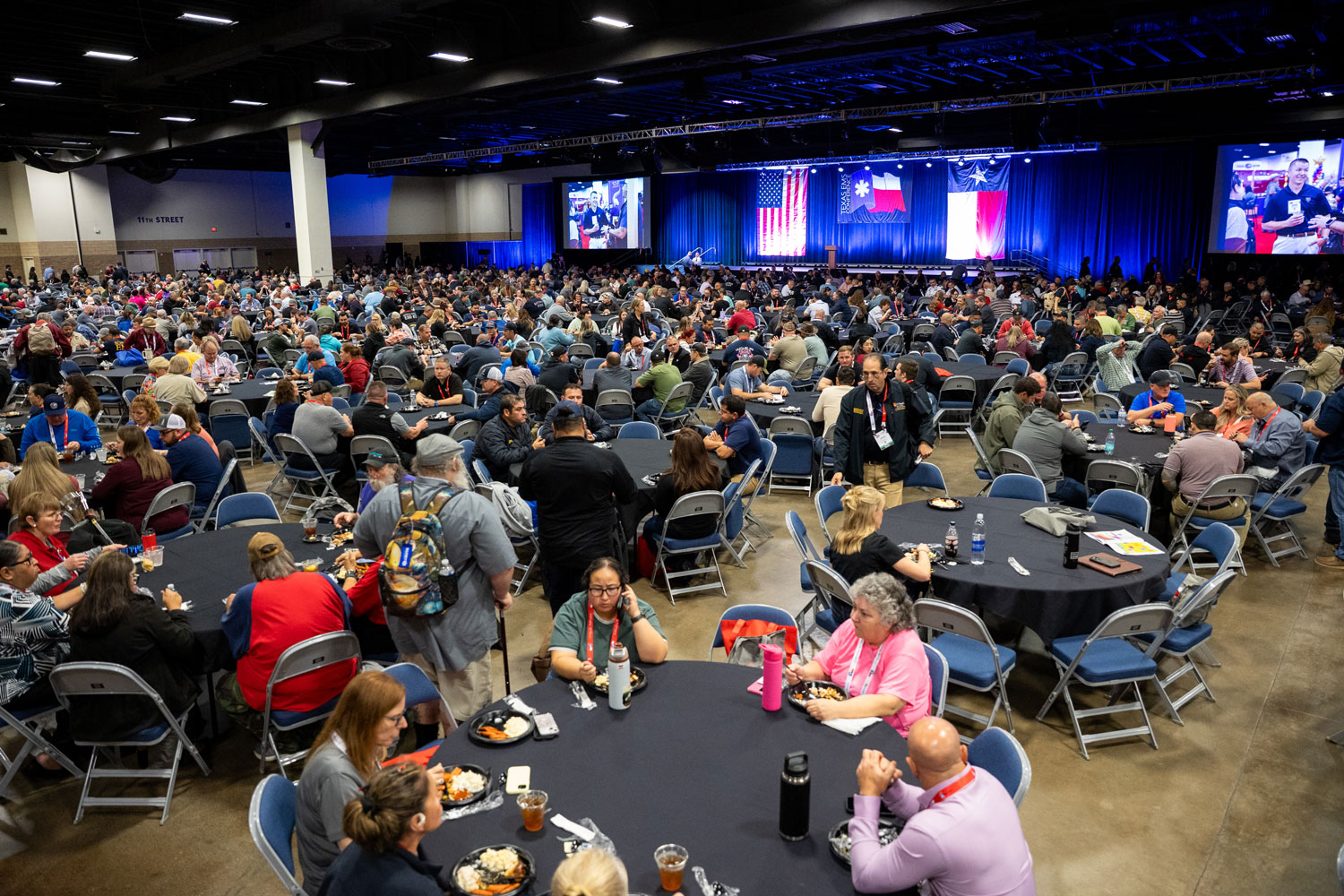 Attendees and exhibitors eating in a large ballroom with stage and screens | Texas EMS Conference